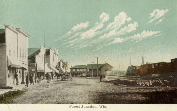 Colorized postcard view of a street scene featuring several storefronts with people in front of them, a horse with a small wagon, telephone poles, and a train. Caption reads: "Forest Junction, Wis."