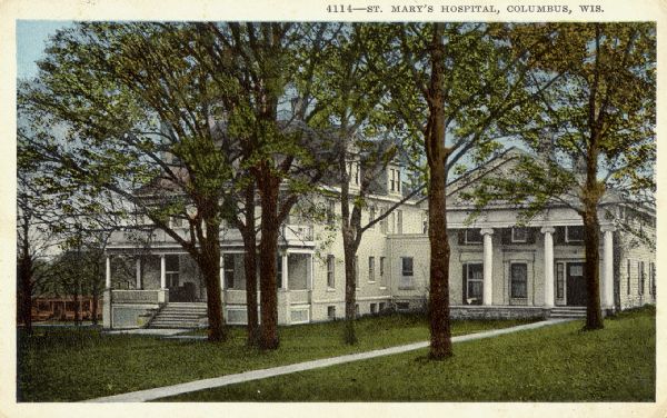 Colorized postcard view across lawn towards a large building, partially obscured by trees. Caption reads: "St. Mary's Hospital, Columbus, Wis."