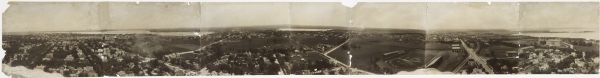 Elevated panoramic view of the city of Madison, with the Wisconsin State Capitol and Lake Monona on the far left, and Picnic Point and Lake Mendota on the far right. The Yawkey-Crowley Lumber Co. building is in the center, with the state fairgrounds just right of the center. The images were probably taken from the chimney of the University of Wisconsin Power Plant. The panoramic was created by connecting 7 panels.