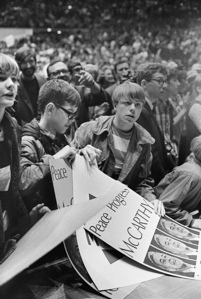 A group of teenage boys are in a crowd of 18,000 people at a Democratic presidential candidate rally for Sen. Eugene McCarthy at the Dane County Memorial Coliseum. They are holding posters which read: "Peace Progress McCarthy for President." The third boy from the left is Eric Anderson.
