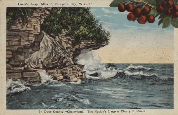 Color postcard across water towards a rock formation. Waves are breaking against the rocks below. In the upper-right corner of the postcard are cherries on a branch. Caption at top reads: "Lover's Leap, Idlewild, Sturgeon Bay, Wis." The bottom of the postcard reads: "In Door County 'Cherryland,' The Nation's Largest Cherry Producer."