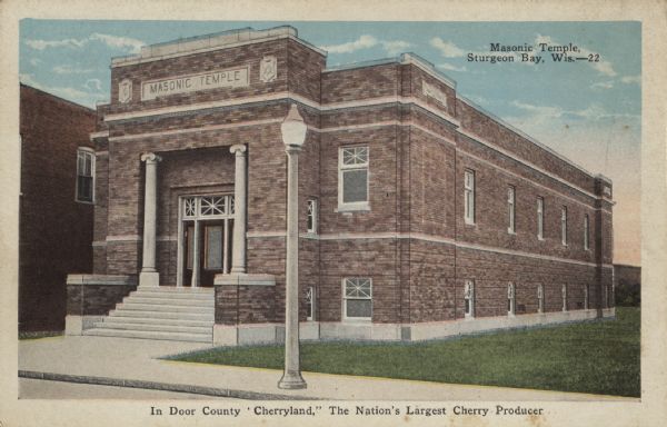 Color postcard showing a two-story brick building with a sign indicating it is a Masonic temple. A streetlight is in front of the building. At the bottom of the postcard is a caption which reads: "In Door County 'Cherryland,' The Nation's Largest Cherry Producer."