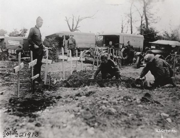 Soldiers adorning the grave of a fallen comrade at the advanced dressing station, the farthest point to which ambulances would travel. A sign on an ambulance in the background on the left reads: "American Red Cross, Outpost Service." Near Juvigny, France.