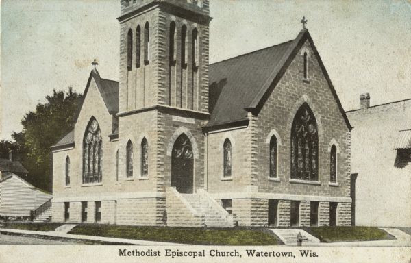 Tinted postcard view across street towards a church on a corner lot. There is a wooden building in the background on the left, and the side of a brick building is on the right. The church tower is partially visible, and stained glass windows are on the front and left side of the church. Caption reads: "Methodist Episcopal Church, Watertown, Wis."
