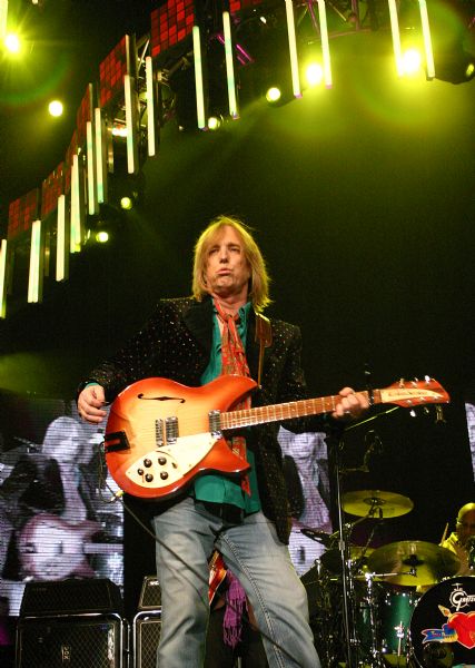 Tom Petty performing at the Alliant Energy Center with his band Tom Petty and the Heartbreakers. There are images of the show on a video screen behind him.