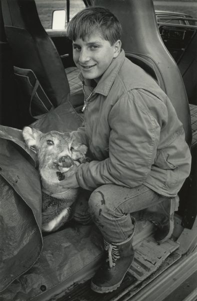 A teenage boy is posing in the back seat of a vehicle with a dead deer, which is partially concealed under a tarp. Caption reads: "FIRST DEER - Ryan Sherman, 15, posed with a doe he shot on opening day of the gun deer hunting season. It was the first time the high school freshman had been deer hunting."