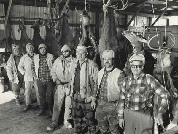 Seven men are posing in a barn with eight killed deer strung up behind them. Caption reads: "SUCCESSFUL HUNT — Every member of this hunting party bagged a deer by 10 a.m. on opening day last Saturday. Standing with their trophies from left to right were George Krejci, Daryl Hoksch, Richard Perkovich, Pete Krejci, Orlyn Hoksch, David Gorell and Carl Lindbo. Sonja Fernholz, not shown, was also a member of the party and shot a deer. The photo was taken at the farm of Orlyn Hoksch in Alma."