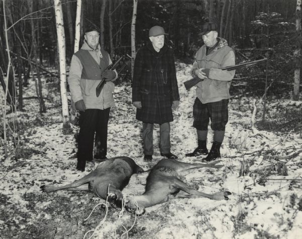 Three men are standing in a clearing, with one man holding a rifle and a the other a shotgun. Two killed deer are lying on the ground in front of them. Caption reads: "Madeline Island, Wis. Autumn 1949. Left to right: W.E. Wagener, Sturgeon Bay Attorney and former backfield member of the University of Wisconsin Football Team, c. 1905; H.C. Scofield, Sturgeon Bay, a prominent local sage, who, upon his death at 93 (29 May 1952), had a record of 81 annual deer hunts in 1951; and 'Cap' Walker (of the Sturgeon Bay <u>Advocate</u>?)."
