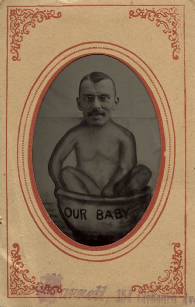 Comedic photograph of a man wearing eyeglasses with a drawing depicting him as a baby in a wash basin, labeled "Our Baby."