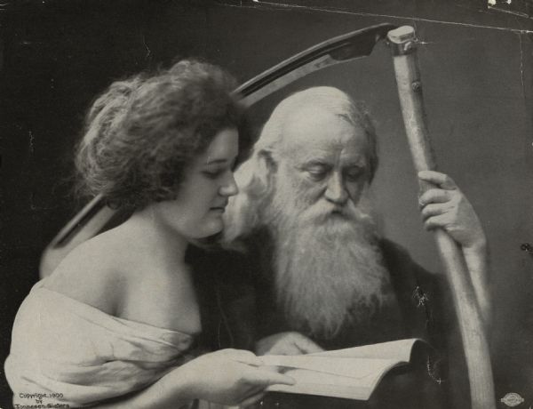 A young woman is holding a book next to a man dressed as Father Time. The man has a long white beard and hair and is holding a scythe.