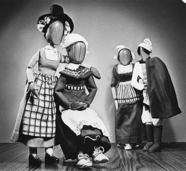 Four dolls are dressed in costumes of unidentified origin. The dolls are wooden and do not possess facial features. The dolls have been posed as two pairs.