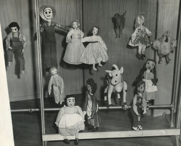 Thirteen puppets, representing a mixture of human and animal shapes, hang by their strings. A caption on the rear of the image identifies them as recreational therapy from an otherwise unidentified "O.T. [occupational therapy] Dept."