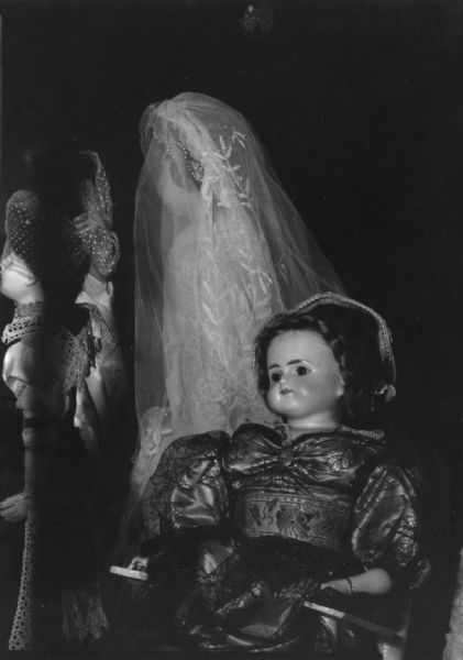 Three dolls are posed together. One is wearing a veil. Caption reads: "19th Century dolls owned by Mrs. Henry A. [Ruth] Pochmann, Madison, in an exhibit in the State Historical Society of Wis. Aug 22 1961 to Dec 11 1961. Photo by Paul Vanderbilt."