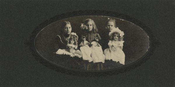 Three girls are posing holding their four dolls. A caption identifies them as: Marguerite H.B. Dennis, Bessie, Charlotte Zaninggers.