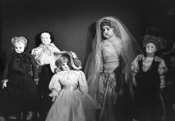 Five dolls are posed together. Two are wearing veils and a third is wearing a hat. Photo caption reads: "19th Century dolls owned by Mrs Henry A. [Ruth] Pochmann of Madison on exhibit in State Historical Society of Wisconsin Aug 22 1961 to Dec 11 1961. Photo by Paul Vanderbilt."