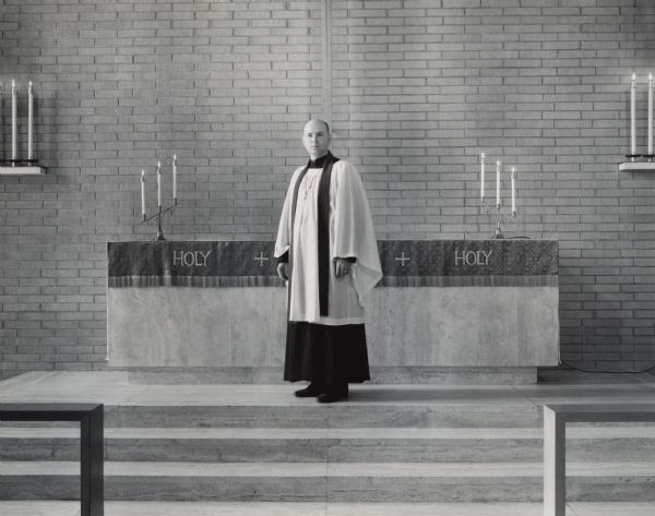 A man is standing and posing in front of a church altar. He is wearing traditional Lutheran vestments: a stole, crucifix, chasuble, and cassock. He is identified in a caption as Rev[erend] Richard L. Buege of St. Luke's Lutheran Church.