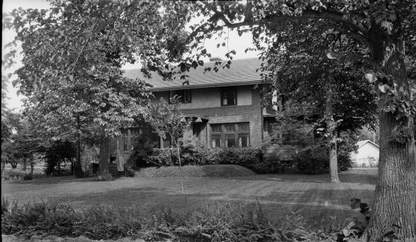 View across lawn towards the Lakewood-Curtiss House at 82 Cambridge Road. A flag is hanging near the front steps under a tree on the left.