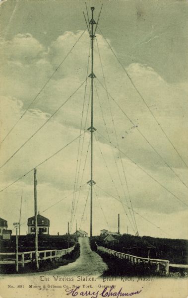 View of Richard Fessenden's radio tower at Brant Rock, Massachusetts. A fence-lined dirt road leads toward the tower and several structures can be seen in the distance. Caption reads: "The Wireless Station. Brant Rock, Mass."