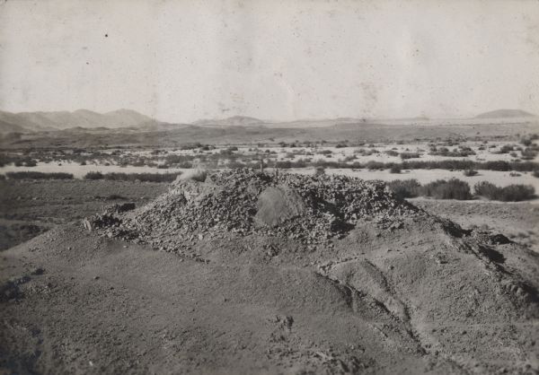 View of the tomb of Queen Tin Hinan from the south. Three people are standing on top of the tomb. Mountains and the city of El Oued can be seen in the background. Caption reads: "14-9 Tomb at Abelessa from south: Note Oued and mountains in the background. November 15, 1925."