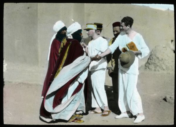 Hand-colored lantern slide showing Count Byron de Prorok, and other members of the Algerian expedition, greeting veiled Algerian men.