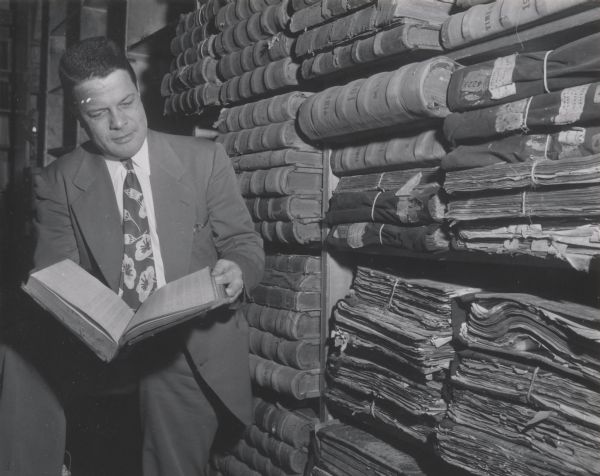State Historical Society of Wisconsin Director, Clifford Lord, posing with a volume from the McCormick collection shelved on the right.