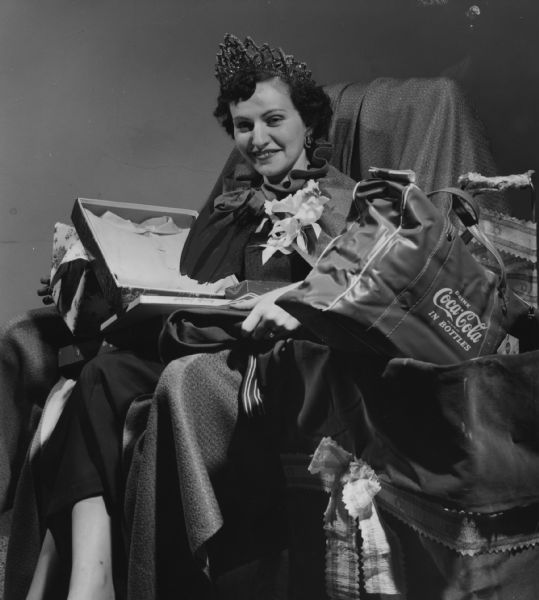A woman is sitting and smiling, and wearing a crown. She is holding an opened package, and next to her is a bag advertising Coca-Cola. Caption reads: "'<b>Queen for a day</b>' Saturday was Mrs. Sherman [Ada] Lefco, 2042 N. 57th St. She won the title by signing up more new members than anyone else in a drive held by the Morris R. Guten Auxiliary 487 of the Jewish War Veterans. Mrs. Lefco was crowned in a ceremony at the Elks club and given a variety of gifts."