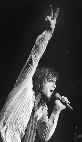 Musician Eddie Money singing and holding up two fingers during a performance. He was opening for the band Cheap Trick.