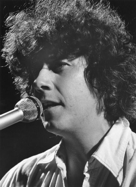 Close-up of Arlo Gurthrie singing into a microphone during a performance.