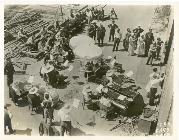 Elevated view of the set of the film "Congress Dances." Everyone, including many musicians wearing large brimmed hats, is gathered outside of a building.