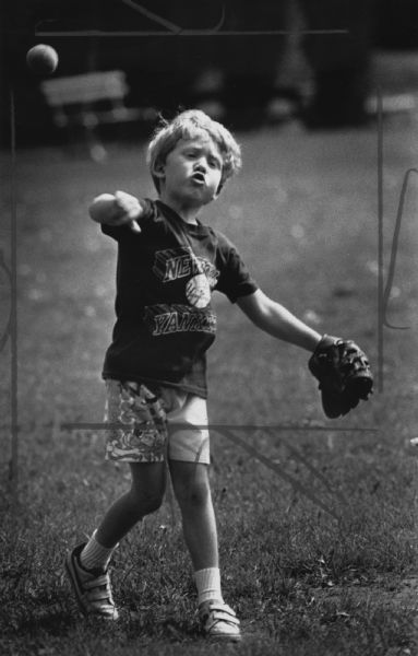 A boy wearing a baseball glove throwing a baseball. Caption reads: "David Friedlander, 4, throws a ball as he plays catch with his father, Gardner, in Klode Park in Whitefish Bay. David was warming up to attend the Milwaukee Brewers game later Tuesday. David said he hoped to catch a foul ball when Milwaukee played Boston."