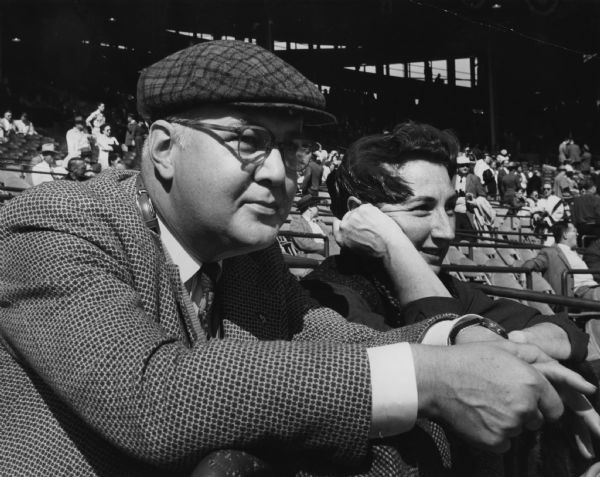 A man and woman sitting in a stadium. Caption reads: "<b>Pleased (to put it mildly)</b> with the way the Braves were playing, Dr. and Mrs. M.A. [Marvin A. and Adelaide] Jochimsen, 2441 N. 96th St., Wauwatosa, just relaxed and enjoyed the fifth game of the world series."