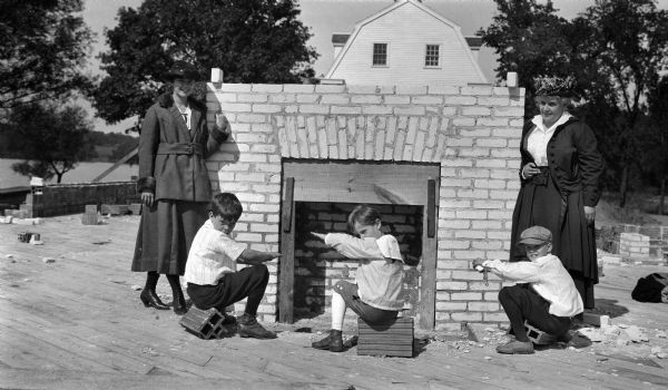 Two women and three children posing by a fireplace during the construction of the Lakewood House.
