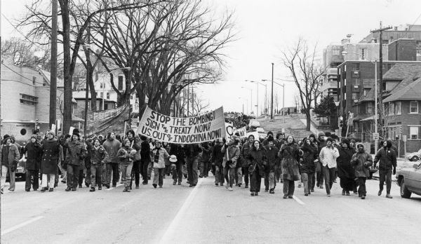 Demonstrators marching up Wisconsin Avenue with a banner that includes the text: "Stop The Bombing! Sign the Treaty Now! U.S. Out of Indochina Now!"