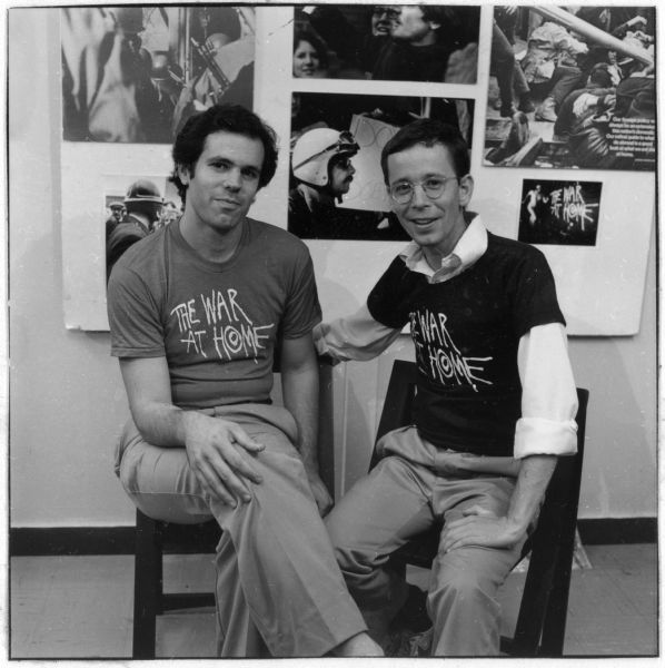The directors of documentary film "The War at Home," Glenn Silber, at left, and Barry Alexander Brown, at right, sit in front of a display of protest images. The images on the display, and their t-shirts are promoting their documentary which depicts protests against the Vietnam War in Madison, Wisconsin.