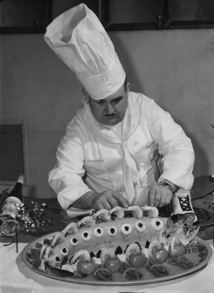 A man in a chef's uniform is preparing a row of shrimp along a cooked salmon on a platter. Caption reads: "A salmon dish decorated with shrimp by Chef Paul Golde of Mader's restaurant."