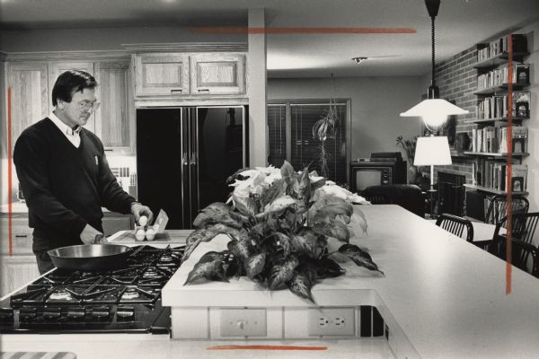A man is standing by a countertop taking an egg out of a carton. Next to him is a stove with six burners and a large pan on it. Caption reads: "Jan Schlabowske, at the stove, says he took some kidding for specifying a six-burner cooktop, but adds that he knew it was worth it the first time he had to use the fifth burner."