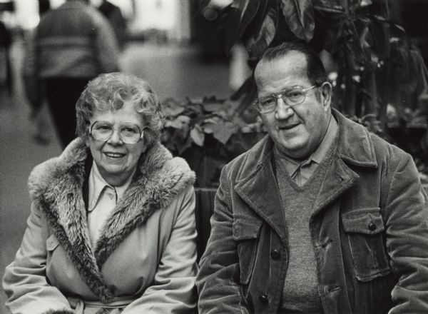 Portrait of a woman and man sitting next to each other. The woman is wearing a fur-lined coat and the man is wearing a corduroy jacket. Caption reads: "<b>Audrey and Richard Ircink</b> Good memories from 1982."