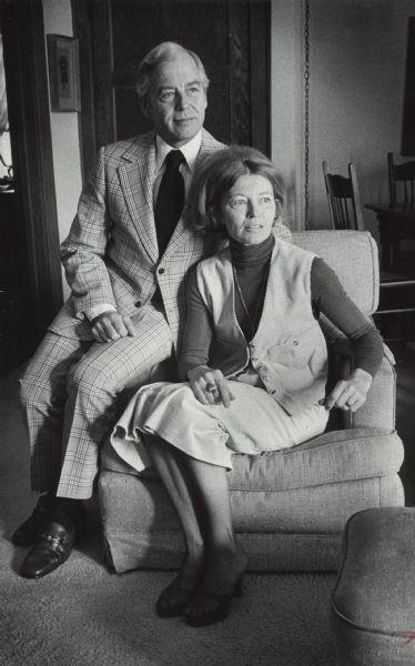 Portrait of a man and a woman sitting together on a chair. Francis, wearing a suit and tie, is sitting on the arm of the chair to the left of Louise, who is wearing a corduroy vest, turtleneck and skirt. Caption reads: "Not surprisingly, Mrs. [Louise] Cerletty makes clothes for both her husband, Francis, and for herself."