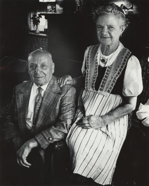 Portrait of a man and woman posing sitting together, with the woman sitting on the arm of the chair. Caption reads: "Hans and Mary Kunzler."