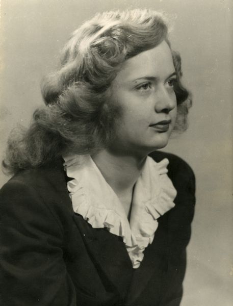 Quarter-length portrait of Marcelaine "Marcy" Hobson (1925-2010) looking to the right. Marcy is wearing a dark suit jacket and a white ruffled collar. Her long, thick hair has been curled and she has on dark lipstick. At the time of this photograph, Marcy was a 19-year-old student at the University of Wisconsin working on her degree in home economics. Her father Asher Hobson was a professor in agricultural economics at the University.