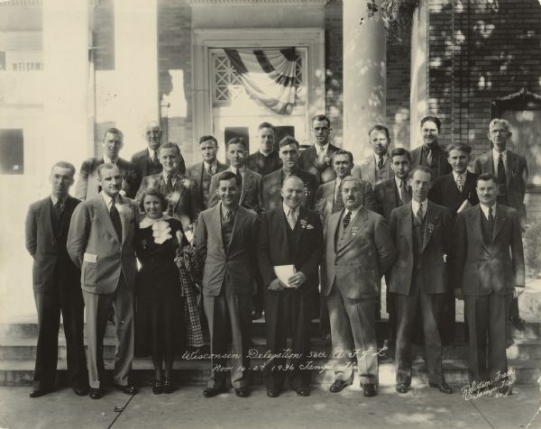 Group portrait of 22 people posing in front of a building. A caption on the back of the image identifies many of the people, though it does not seem to account for everyone. It reads: "Wisconsin Delegation, 56th A.F. of L. Convention. Nov. 16-27, 1936. Tampa, Florida. Front row left to right: Felix Olkines, Kenosha; Mabel Melvin, Wausau; Emil Costello, Kenosha; Stanley Joers, Milwaukee; Joseph A. Padway; Erwin Zumach, Milwaukee; Steve J. Thomas, Racine.
Second row left to right: August J. Scherr, Milwaukee; Cedric Parker, Madison; Andrew B. Cross, Kenosha; Joseph M. Driscoll, Milwaukee; David Sigman, Two Rivers; Robert W. Powers, Port Washington; Rudolph Faupl, Milwaukee.
Third row left to right: Charles Heymanns, Sheboygan; John J. Handley, Miklwaukee; J. F. Friedrich, Milwaukee; Father Francis J. Haas, Milwaukee; Arnold S. Zander, Madison; Henry Rutz, Milwaukee; Paul Porter, Kenosha; and William H. Sommers, Racine."