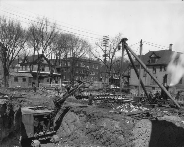 Orpheum Theater construction, 216 State Street, looking north with steam shovel. Also shows Holy Redeemer Catholic Church, 128 W. Johnson Street, and Holy Redeemer Rectory, 120 W. Johnson Street, and Windemere Apartments, 118 W. Johnson Street.