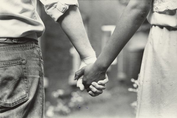 Close-up of two people holding hands, one white and one black. Caption reads: "Black-white couples say that racial difference is no big deal for them, but that others are sometimes curious or even downright hostile."