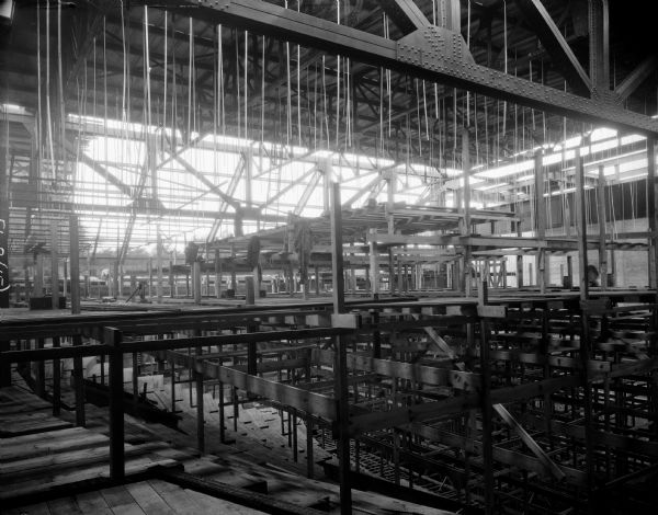 Orpheum Theater under construction, 216 State Street, from upper balcony. A man looking up at the ceiling rafters is standing on top of scaffolding in the center. Below him coats are hanging from the scaffolding. Another man (blurred from movement) is working on the balcony on the far right. Caption reads: "Orpheum Theatre, Madison, Wisconsin, Beecroft Bldg. Co., Builders; C.W. & Geo. L. Rapp, Architects; A.D. & J.V. Fredrickson, Contractors."