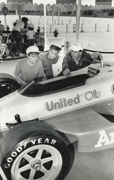 Two boys and a man are looking into the cockpit of a race car. Caption reads: "A CLOSE LOOK — David Berner (left), 11, of West Allis, and Jay Gmeindl, 9, of Greendale looked over Scott Brayton's Indy car recently at a County Executive Tailgate for Kids Party at County Stadium. The event was held to raise money for the child abuse prevention fund."