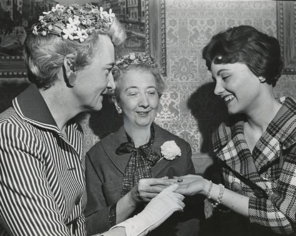 Two older women admiring a pin held by a younger woman. Caption reads: "<b>A small diamond pin</b> which the Gamma Phi Betas at the University of Wisconsin--Milwaukee hope will be coveted by all of its members was admired by (from left) Miss Charlotte Wollaeger, 2428 E. Bradford Av., dean of women at UWM; Mrs. Robert E. Fitzgerald, 1556 Martha Washington Dr., Wauwatosa, past grand president of the sorority, and Miss Cora Leach, Hartford, president of the new Gamma Gamma chapter of Gamma Phi Beta. Mrs. Fitzgerald received the pin in 1946 for her work with the sorority. In the future, it will be given to the junior Gamma Phi Beta who maintains the highest scholastic average during her first three years at college. The UWM chapter of Gamma Phi Beta was installed in festivities last weekend in Madison and Milwaukee. The chapter grew out of Lambda Phi Chi, a local sorority.