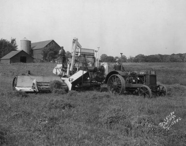 Two men are posing on a Nichols & Shepard combine thresher and Hart Parr tractor.