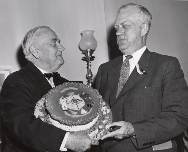 Congressman Alexander Wiley, at left, and another man on the right, holding a cake decorated with the Great Seal of the State of Wisconsin.