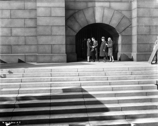 Long shot of Eleanor Griffith, Chester Morris, Harry Stubbs and Mae Busch standing on the steps in front of a prison gate in a scene from the 1929 film "Alibi." Griffith and Morris are looking into each other's eyes, while Stubbs and Busch are looking on. Busch has her hand on Stubbs' arm.