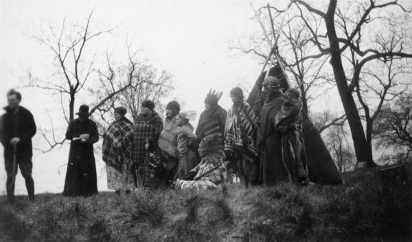 A group of actors, some in Native American clothing, are posing by an Indian lodge. They are participants in a reenactment of a ceremony in which Nicolas Perrot claimed the territory of the upper Mississippi River for France at Fort St. Antoine. 